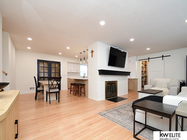 living room featuring visible vents, recessed lighting, light wood-style floors, a barn door, and a brick fireplace