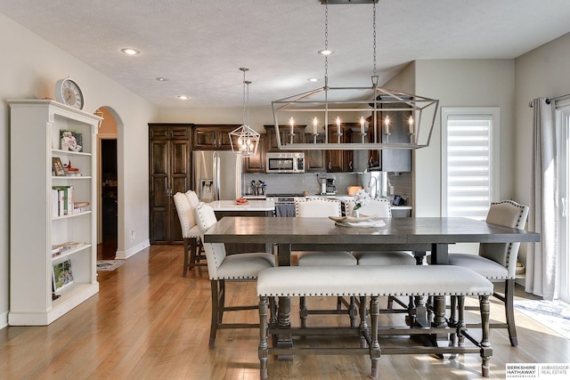 dining space with baseboards, an inviting chandelier, arched walkways, light wood-style floors, and a textured ceiling