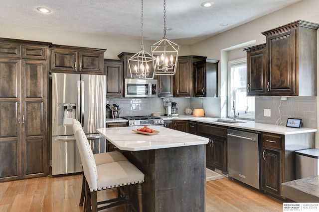 kitchen featuring dark brown cabinetry, appliances with stainless steel finishes, light wood-style floors, hanging light fixtures, and a notable chandelier