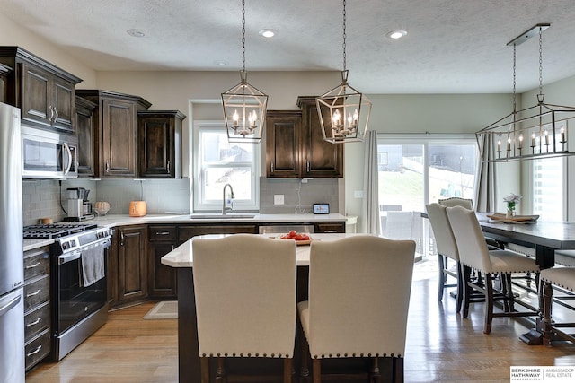 kitchen with an inviting chandelier, a sink, light countertops, dark brown cabinetry, and appliances with stainless steel finishes