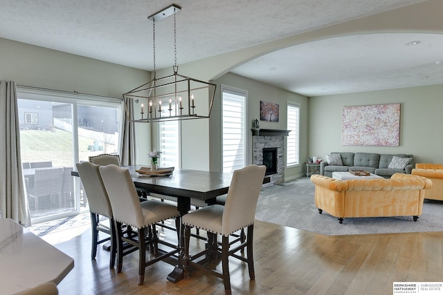 dining room featuring a stone fireplace, wood finished floors, arched walkways, a notable chandelier, and a textured ceiling