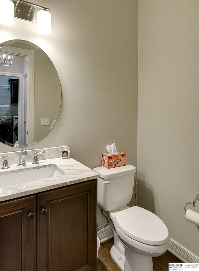 half bathroom with vanity, wood finished floors, baseboards, washer and dryer, and toilet