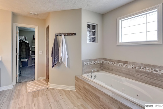 bathroom with visible vents, a textured ceiling, a walk in closet, and a whirlpool tub