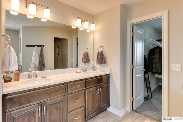 full bath featuring double vanity, a textured ceiling, a walk in closet, and a sink