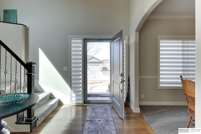 foyer entrance featuring baseboards, arched walkways, ornamental molding, and stairs