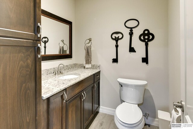 half bath with baseboards, toilet, wood finished floors, and vanity