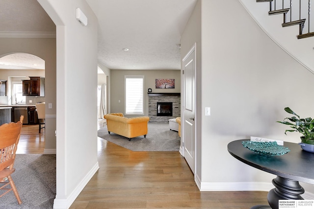 hall with stairway, light wood-style flooring, baseboards, and arched walkways