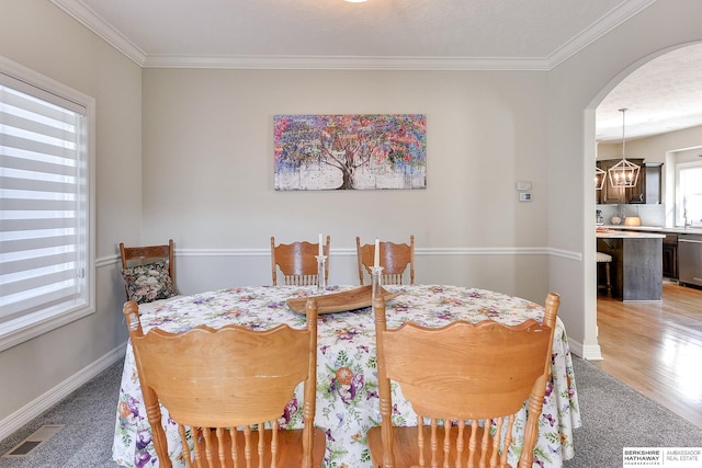 dining room with visible vents, crown molding, baseboards, light wood-style flooring, and arched walkways