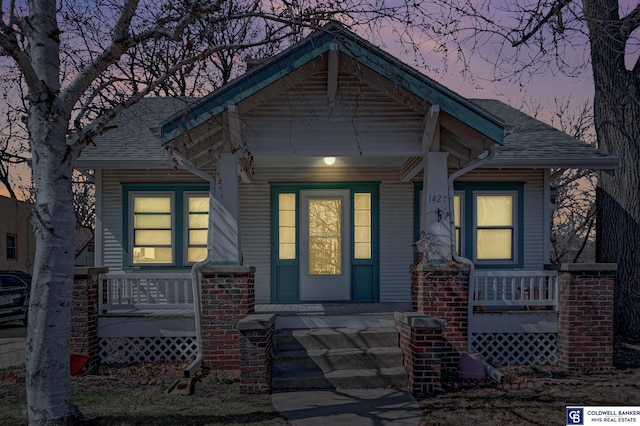 view of exterior entry with a porch and a shingled roof