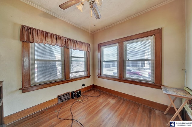 interior space with wood finished floors, a ceiling fan, visible vents, baseboards, and crown molding