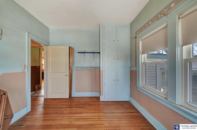 unfurnished bedroom with wallpapered walls, light wood-style flooring, baseboards, and a closet