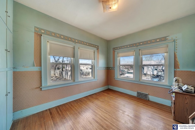 unfurnished room featuring visible vents, baseboards, hardwood / wood-style floors, and wallpapered walls