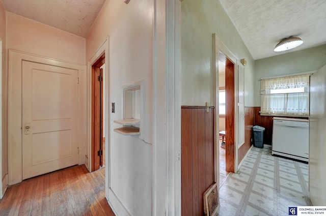 hallway featuring visible vents, a wainscoted wall, light floors, wood walls, and a textured ceiling