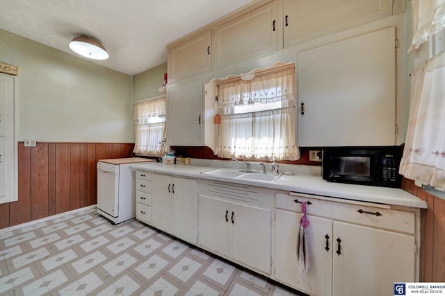 kitchen featuring light floors, a wainscoted wall, a sink, wood walls, and black microwave