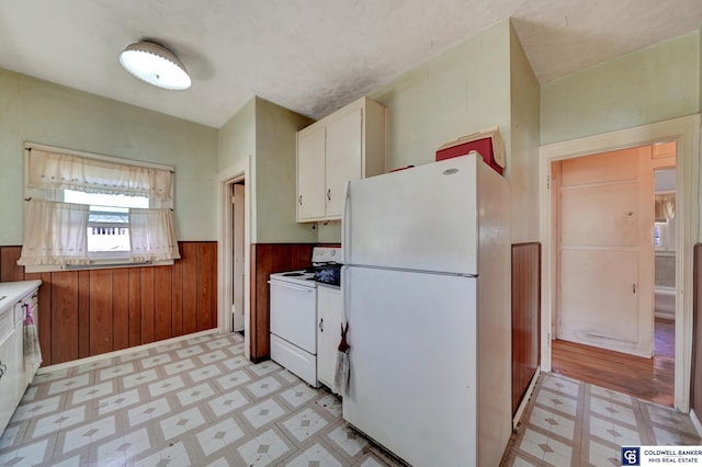 kitchen featuring wooden walls, light floors, wainscoting, white appliances, and white cabinetry