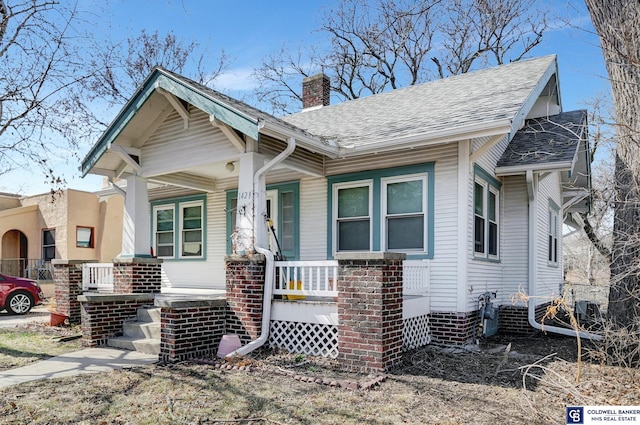 bungalow-style home featuring roof with shingles, a porch, and a chimney