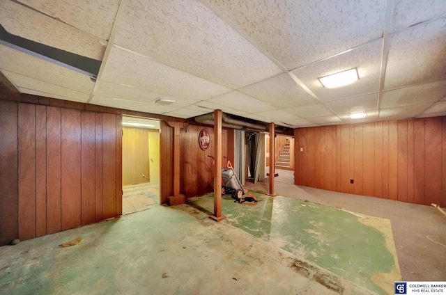 finished basement with a drop ceiling, wooden walls, and stairs