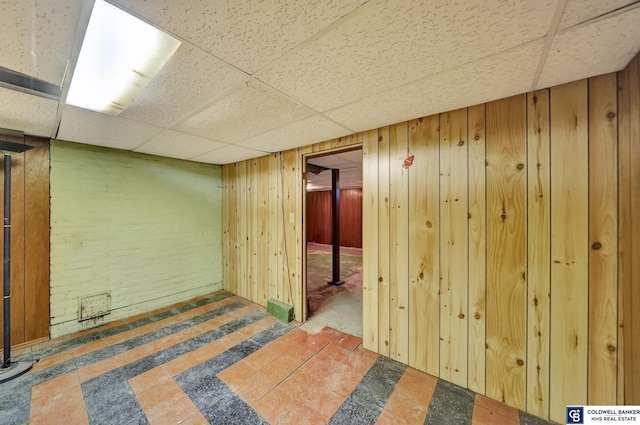 finished basement featuring a paneled ceiling and wood walls