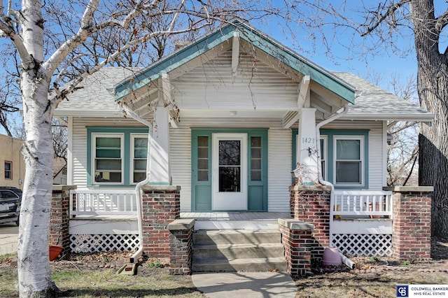 doorway to property featuring covered porch and a shingled roof