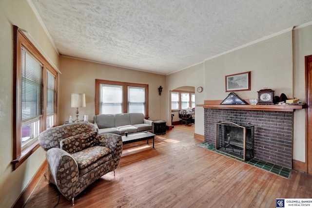 living area with hardwood / wood-style floors, arched walkways, a fireplace, crown molding, and baseboards