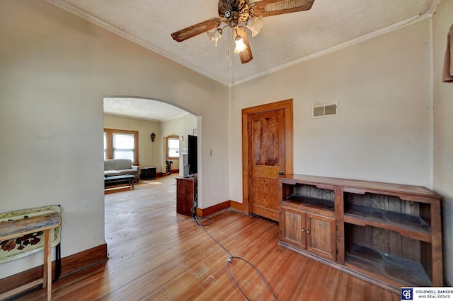 interior space featuring visible vents, arched walkways, ceiling fan, light wood-style floors, and crown molding