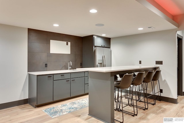 kitchen featuring light wood-type flooring, stainless steel fridge, a breakfast bar area, and light countertops