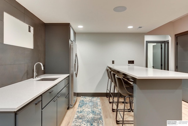 kitchen with gray cabinetry, a breakfast bar, light wood-style flooring, a peninsula, and a sink