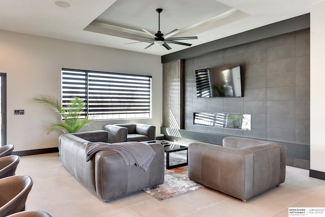 living room with tile patterned flooring, a tray ceiling, baseboards, and ceiling fan