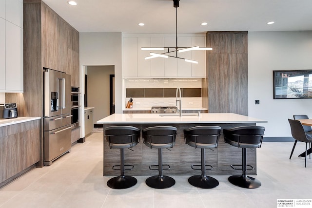 kitchen with a breakfast bar area, a sink, appliances with stainless steel finishes, modern cabinets, and tasteful backsplash