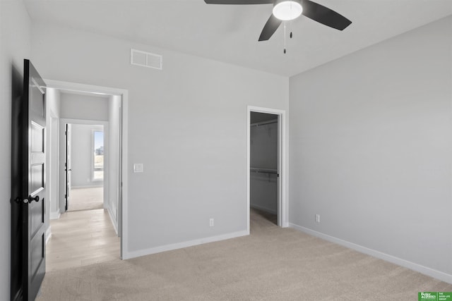 unfurnished bedroom with a spacious closet, baseboards, visible vents, and light carpet