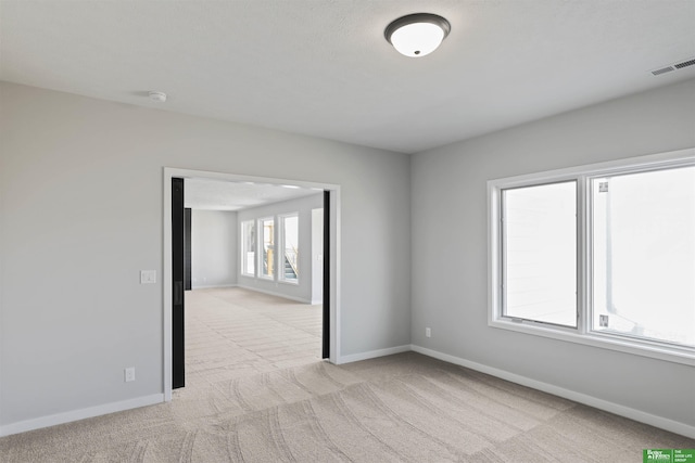 empty room featuring light carpet, visible vents, and baseboards