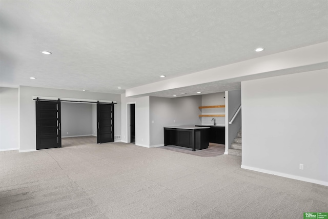 finished below grade area with a textured ceiling, recessed lighting, a barn door, baseboards, and light colored carpet