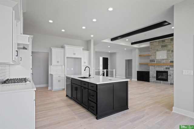 kitchen featuring a kitchen island with sink, stainless steel appliances, a sink, white cabinetry, and dark cabinets