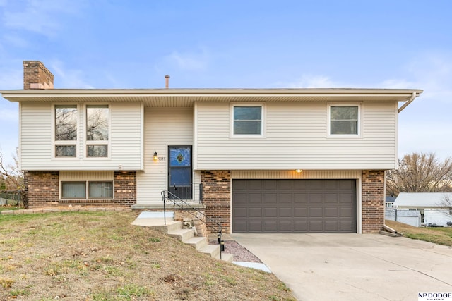 bi-level home with a garage, brick siding, concrete driveway, and a chimney