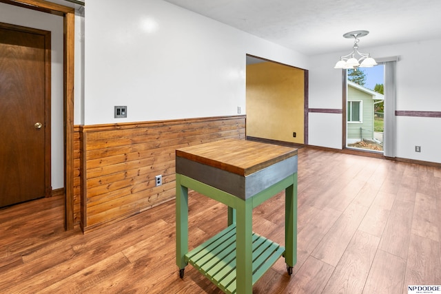 dining space featuring a chandelier, a wainscoted wall, wooden walls, and wood finished floors