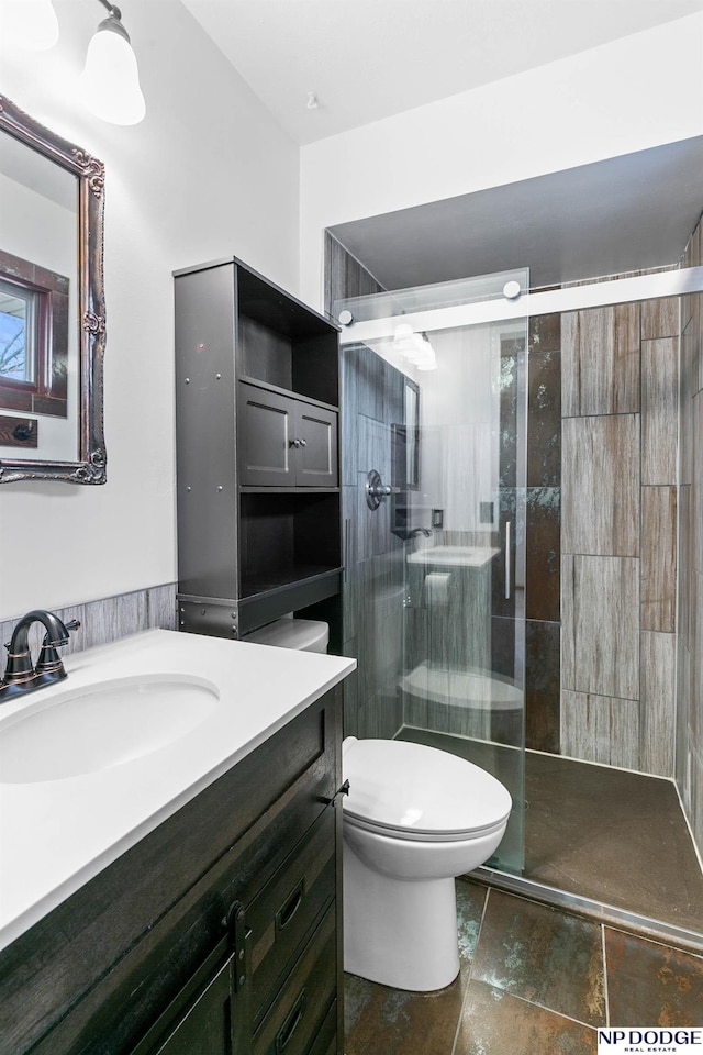 bathroom with stone finish flooring, toilet, a stall shower, and vanity