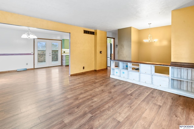 unfurnished living room with a notable chandelier, baseboards, visible vents, and wood finished floors