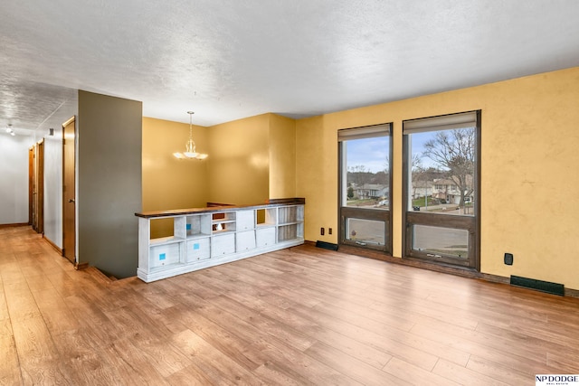 interior space featuring wood finished floors, baseboards, visible vents, a textured ceiling, and a chandelier