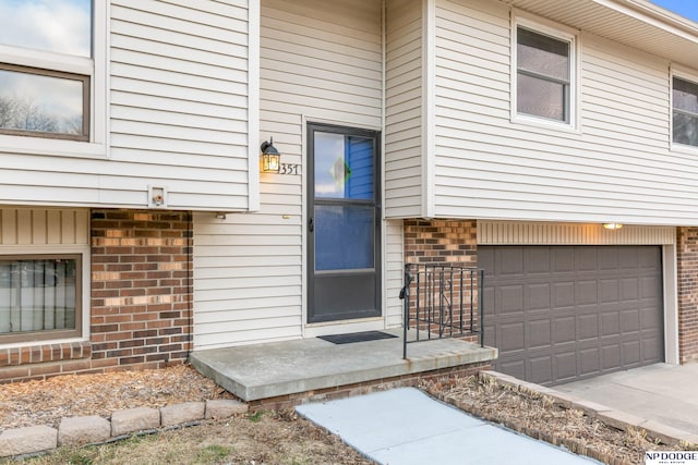 doorway to property with a garage, brick siding, and driveway