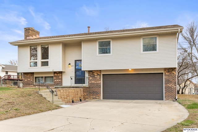 bi-level home with brick siding, driveway, a chimney, and an attached garage