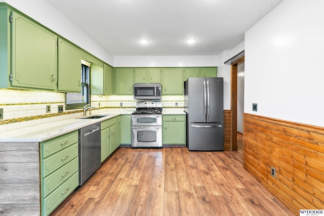 kitchen featuring wood finished floors, a wainscoted wall, a sink, light countertops, and appliances with stainless steel finishes