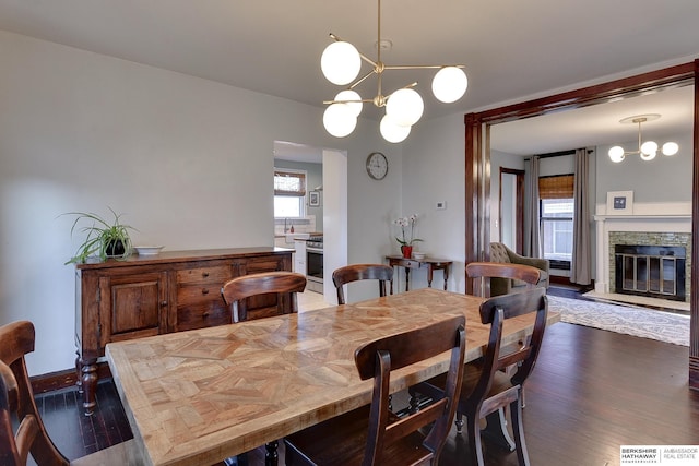 dining space featuring a stone fireplace, wood finished floors, baseboards, and a chandelier