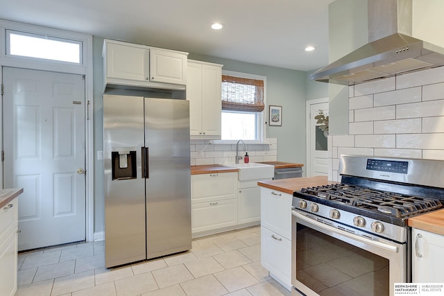 kitchen with a sink, stainless steel appliances, wood counters, white cabinetry, and wall chimney exhaust hood