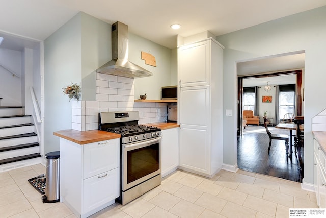 kitchen with wood counters, range hood, white cabinets, decorative backsplash, and gas range