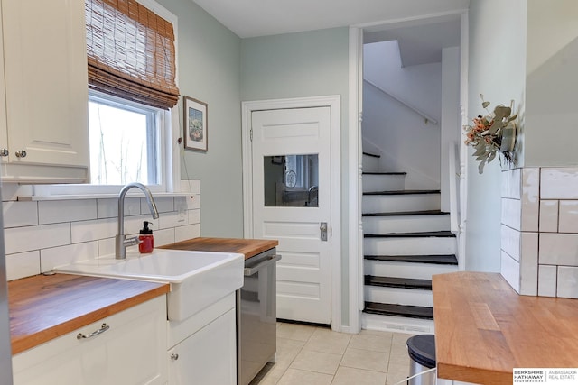 kitchen featuring wooden counters, light tile patterned floors, decorative backsplash, white cabinets, and a sink