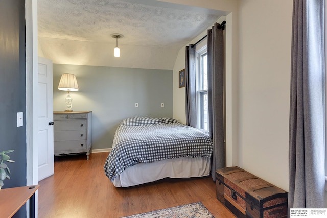 bedroom with vaulted ceiling, a textured ceiling, baseboards, and wood finished floors