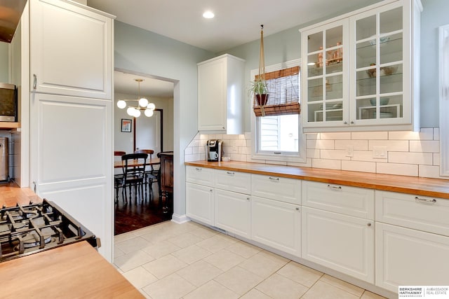 kitchen featuring butcher block countertops, range with gas stovetop, backsplash, glass insert cabinets, and a chandelier