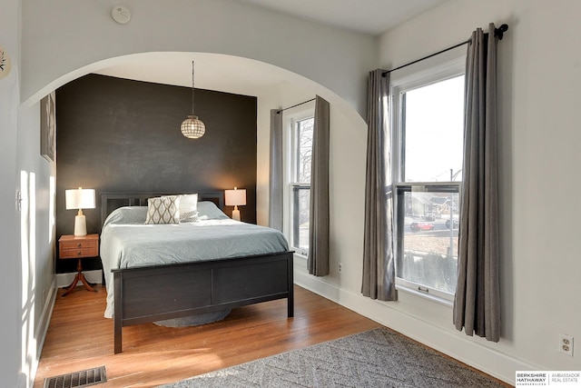 bedroom with wood finished floors, visible vents, arched walkways, and baseboards