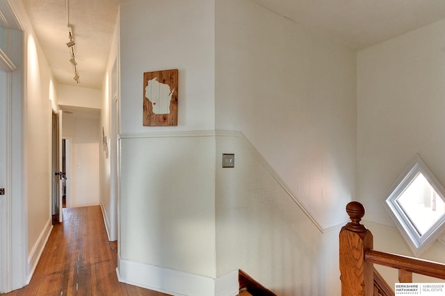 hall with wood finished floors, rail lighting, and an upstairs landing