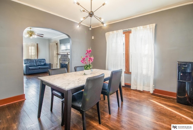 dining area with baseboards, dark wood finished floors, a fireplace, arched walkways, and ornamental molding